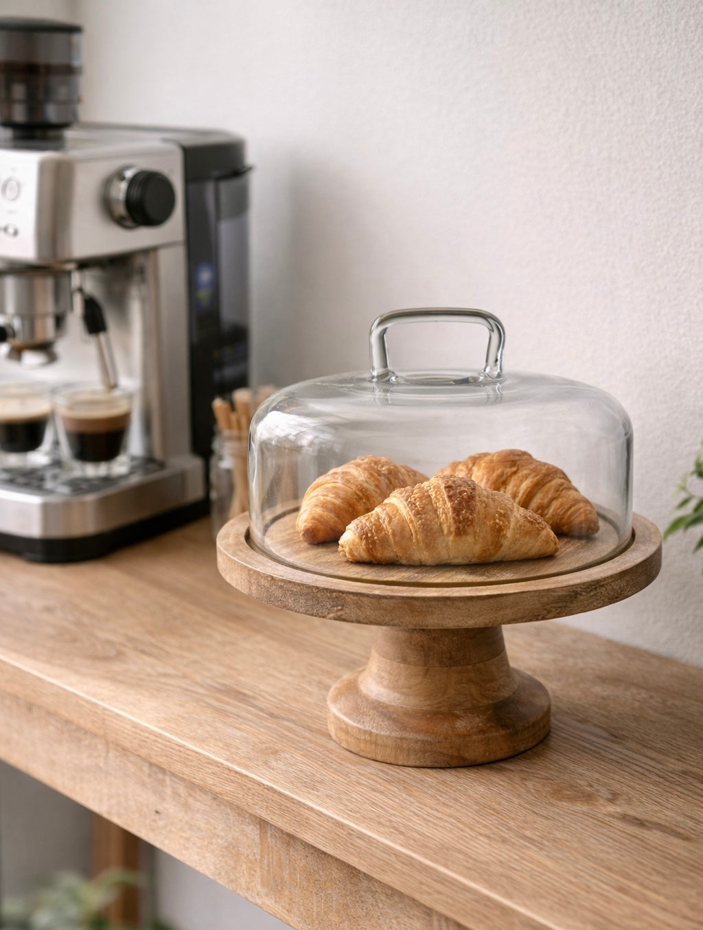 מעמד עוגה מעץ טבעי עם פעמון זכוכית עם קרואסונים לצד מכונת קפה - כלי הגשה מעוצבים להגשת עוגות וקינוחים