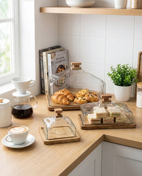 סט כלי הגשה מעוצבים עם מכסי זכוכית ובסיס עץ במטבח על בוצר עץ עם סנדוויצ'ים וקרואסונים