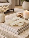 פסל קשר Ivory Loop בצבע שמנת עם ברק עדין על שולחן קפה בעיצוב מודרני