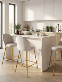 כיסא בר מרופד בד בהיר עם גב מעוגל ובסיס מתכת זהב, מסודר סביב אי עץ במטבח מודרני בהיר