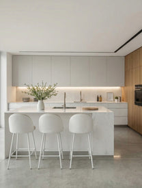 כיסא בר מרופד בד בהיר עם גב מעוגל ובסיס מתכת לבן, מסודר סביב אי במטבח מודרני בהיר